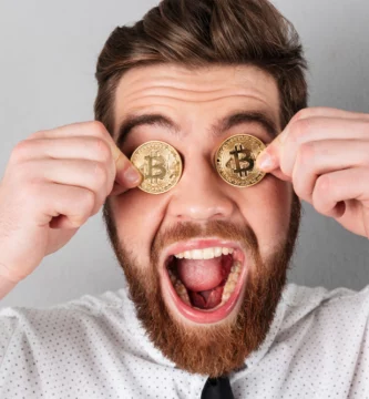 Hombre sonriente sostiene tokens de criptomonedas frente a sus ojos, representando una de las meme coin 2025
