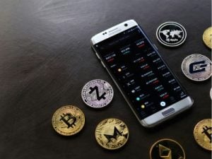 Smartphone con un gráfico de criptomonedas rodeado de criptomonedas fisicas