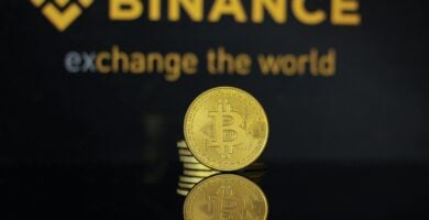 Moneda de Bitcoin con el logo de Binance de fondo