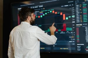 hombre señalando una pantalla de tradin, grafico de velas japones. imagen de stock sobre si es rentable el trading de criptomonedas