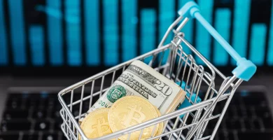 fotografia de un carrito de compras miniatura cargando un billete de dolar y un token de btc para respresentar por que la criptomoneda tiene valor