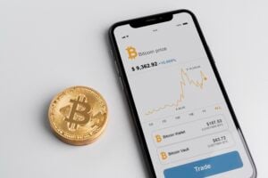 Token de BTC al lado de un smartphone con una app de precio de btc. Como comprar criptomonedas en bbva