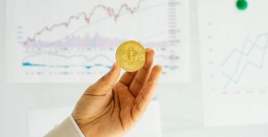 Mano sosteniendo Token de Bitcoin, en el fondo se ve la pizarra de proyecto ¿Qué es un whitepaper crypto? Guía completa. Imagen de stock.